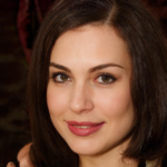 A woman with shoulder-length brown hair and green eyes is smiling slightly at the camera.
